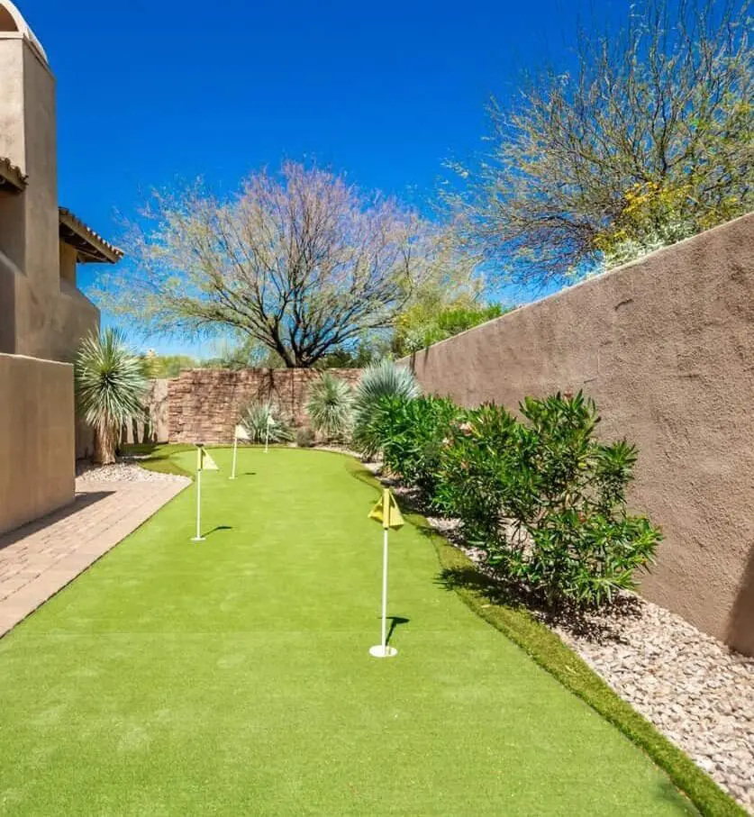 Artificial grass putting green in Surprise AZ that has just been installed by Surprise Artificial Grass Co. Yellow flags in each of the three holes. Green artificial turf green with longer blade height artificial turf on the fringes