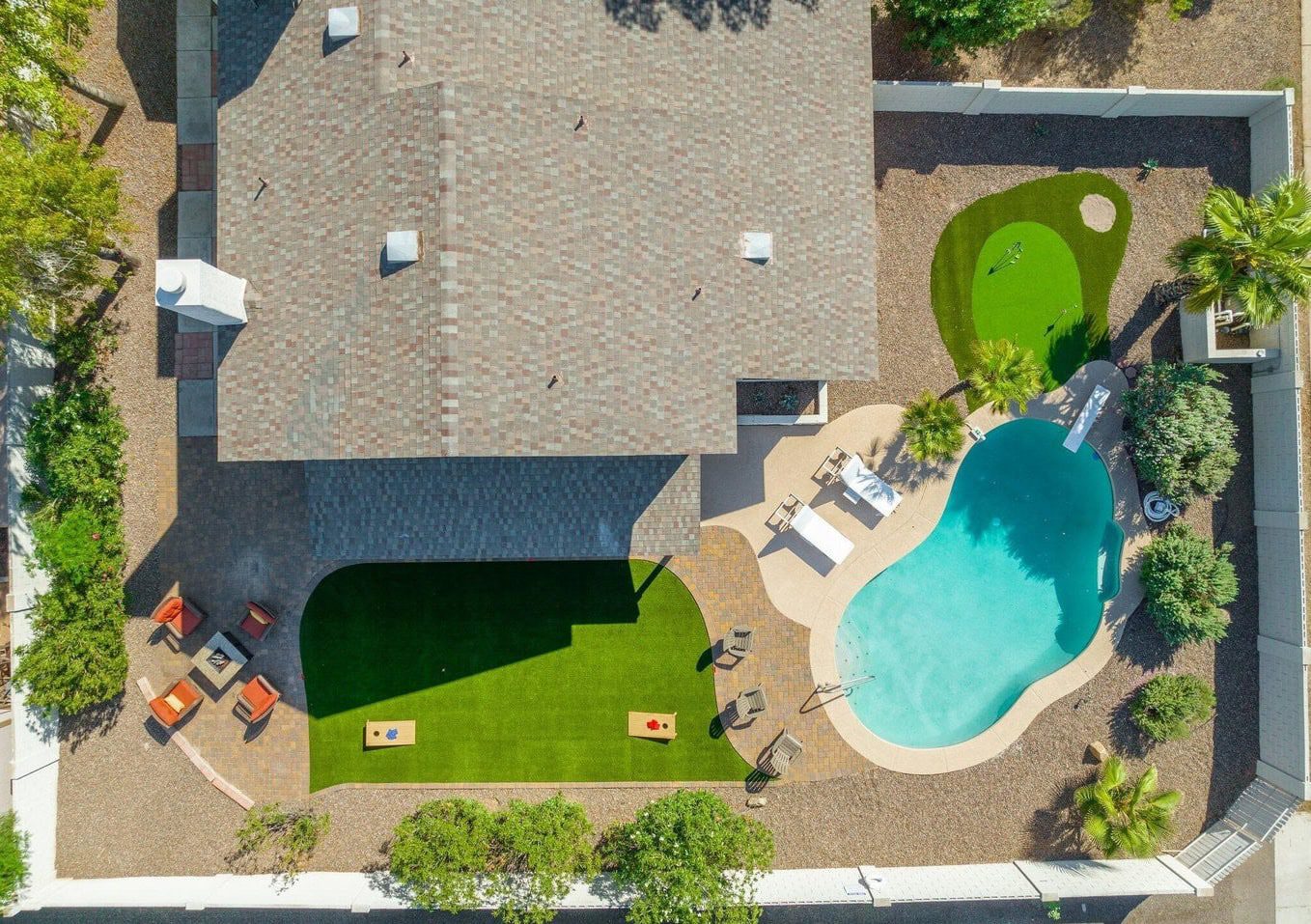 birds eye view of a landscape makeover next to a home in Surprise Arizona. Features green artificial grass, surrounded by pavers, with a blue kidney shaped pool in the corner.