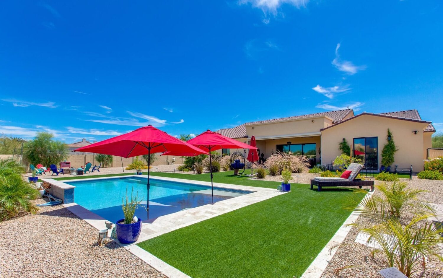 artificial grass pool deck with natural stone pavers around a pool with two umbrellas at a home in Surprise Arizona