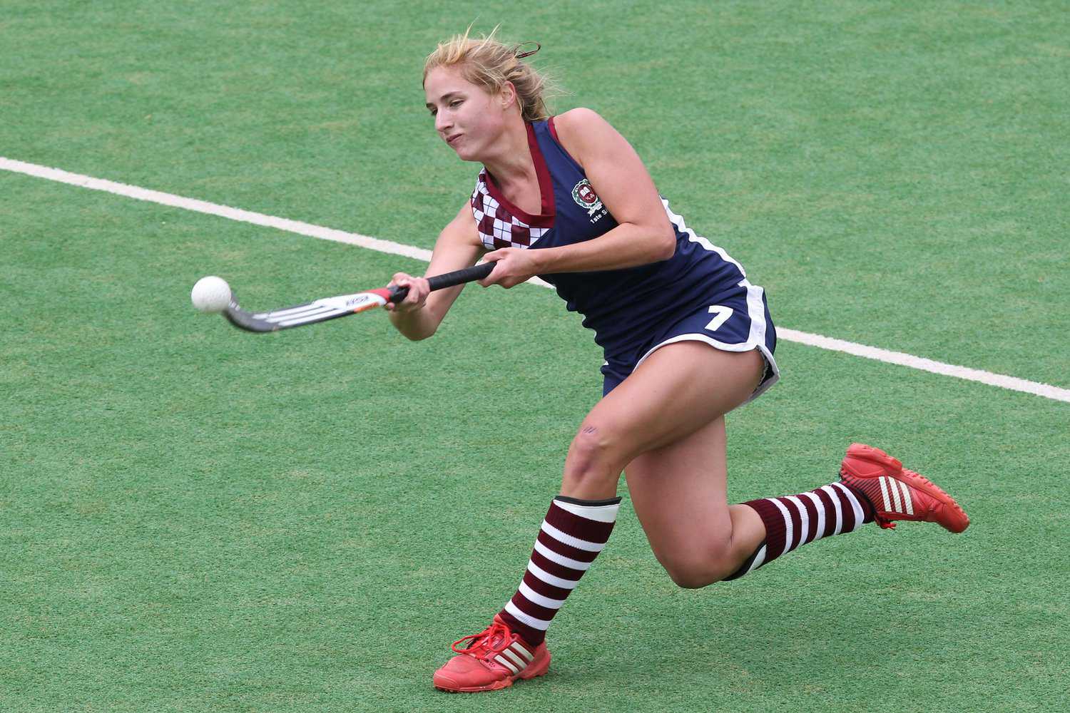 A field hockey player hitting a ball in the air while playing on a synthetic field hockey field that was built by Surprise Artificial Grass Co